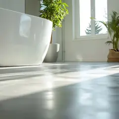 Ett modernt badrum med fristående badkar och gröna växter. Solstrålar lyser upp golvet, som ser ut att vara en våtrumsmatta som är lätt att måla om.